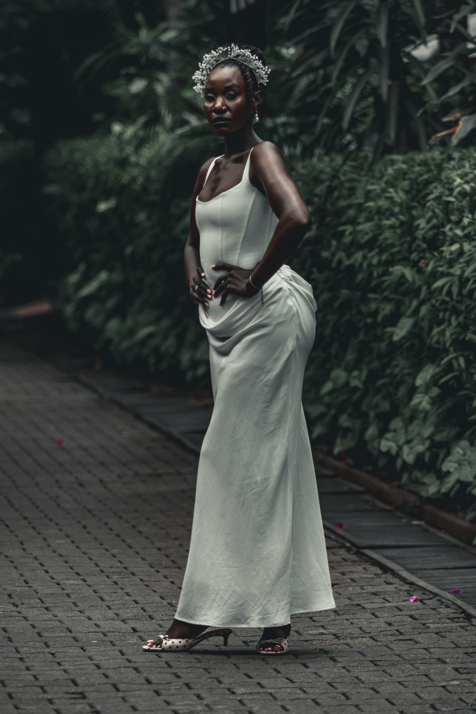 Bride in a white corset column gown and pearl crown on a garden path, side view